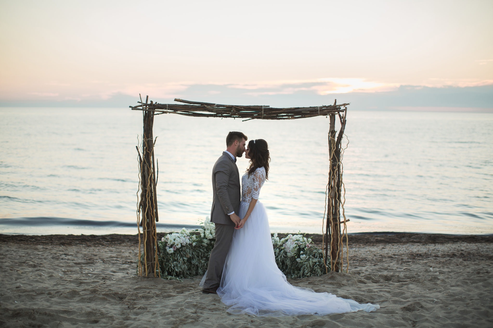 bride and groom under archway on beach.