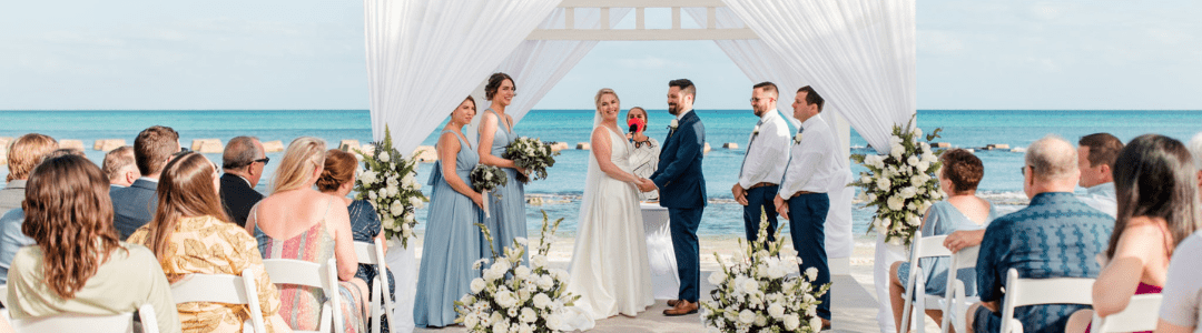View from the back of a destination wedding with guests sitting in chairs and the bridal part at the arch overlooking the water