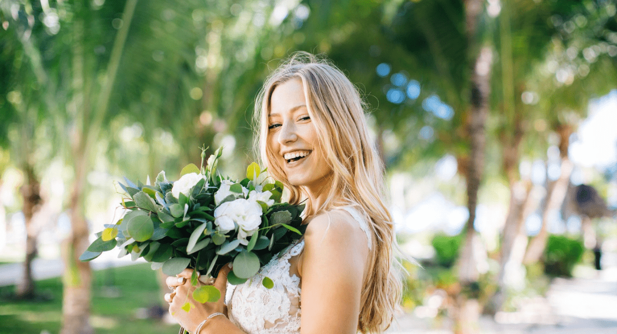 A bride standing in a garden smiling with her wedding bouquet