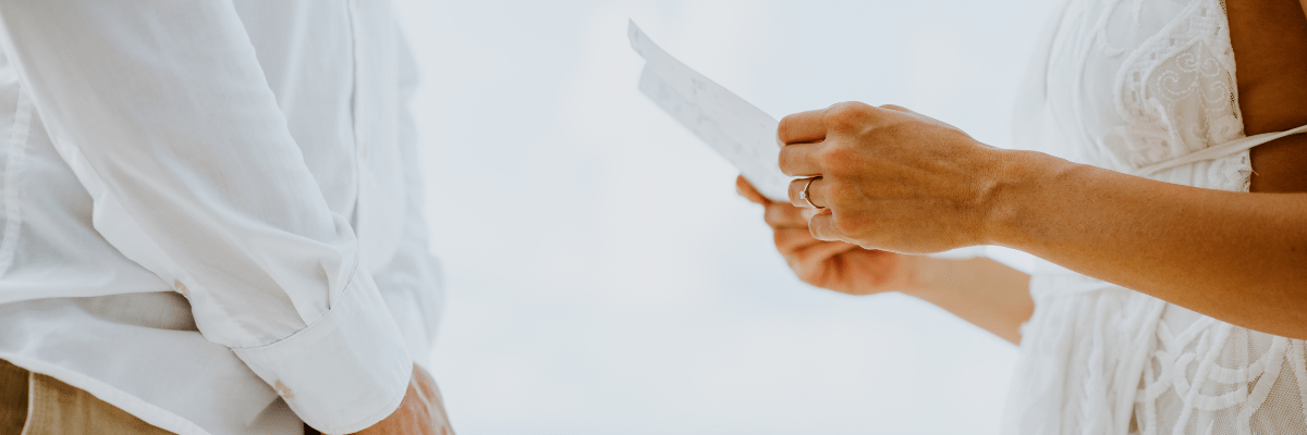 Close up of a woman holding her vows on her wedding day with her husband standing facing her