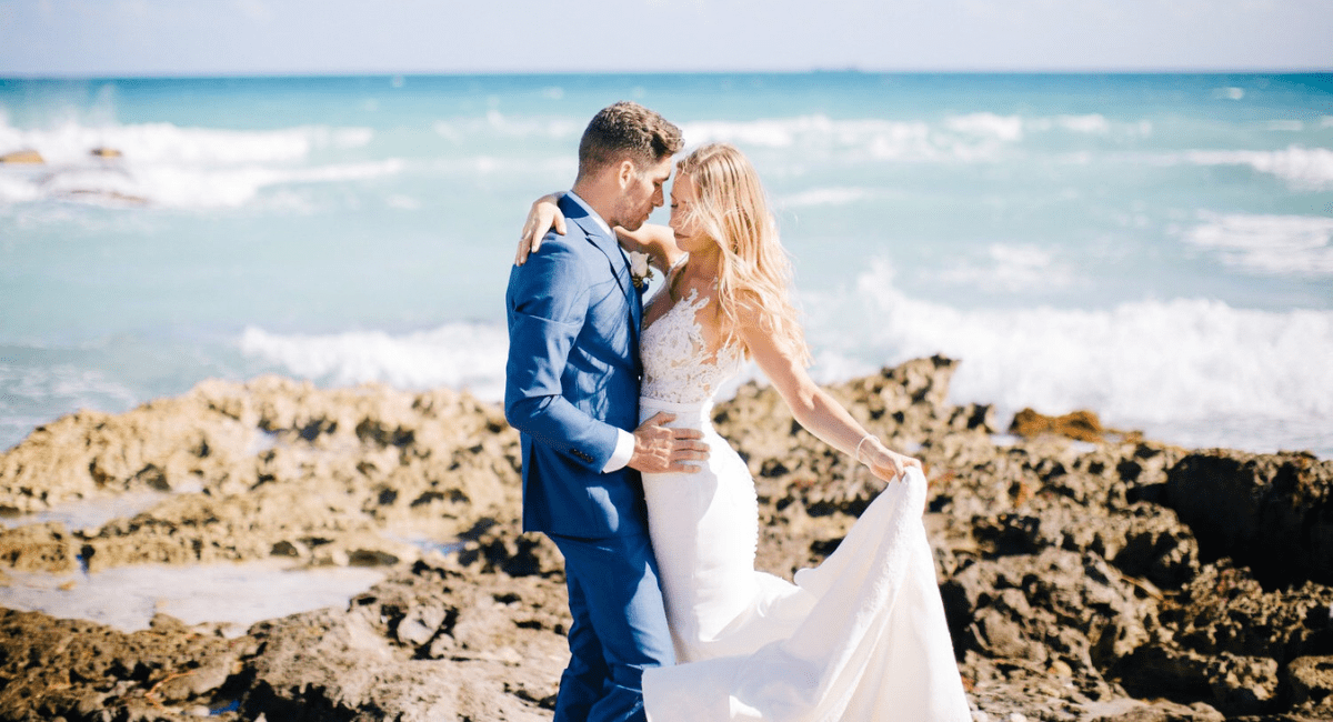 January Header Man and women in their wedding attire posting in front of the water at a destination wedding while standing on rocky ground