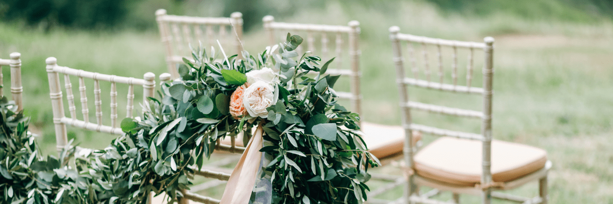 Close up of chairs at a destination wedding with a green leafy garland with small flower accents