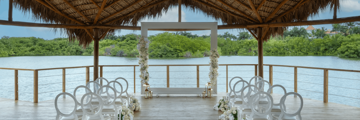 An over the water gazebo setup at a destination wedding with a square backdrop and elegant chairs on a wood floor