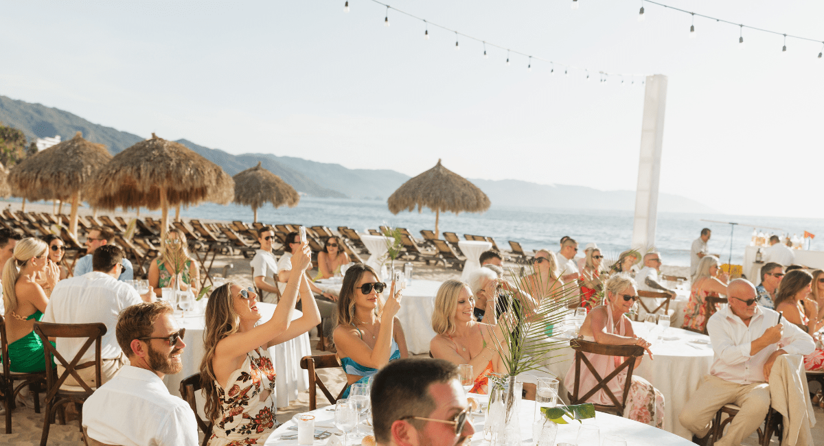 Wedding guests holding their phones up to take photos or record while sitting at their tables at the destination wedding.
