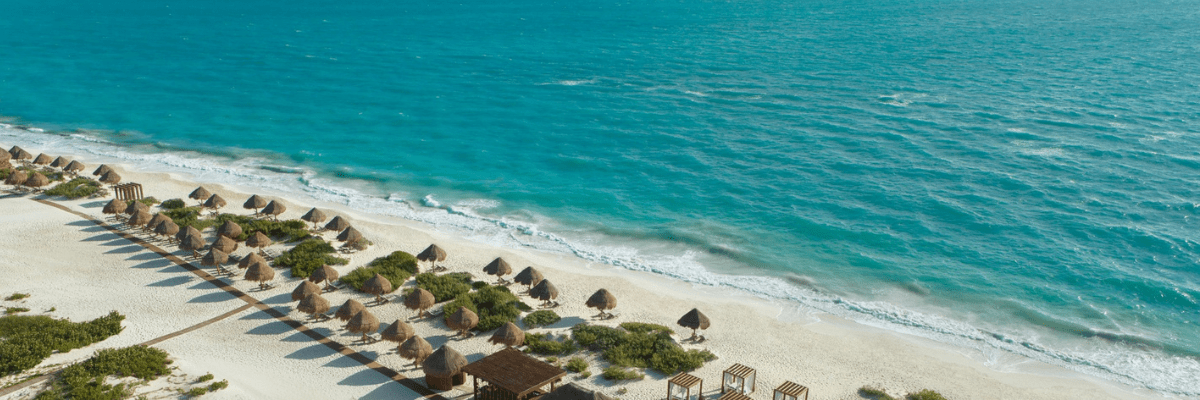 Wide view of a tropical beach and calm ocean at an all-inclusive resort hosting a wedding room block.