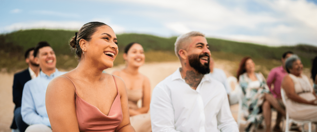 Smiling destination wedding guests enjoying a beach ceremony